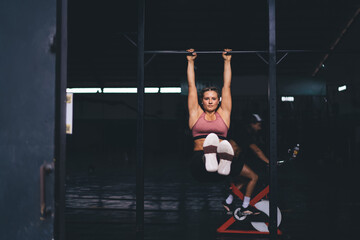 Strong female bodybuilder doing pull-ups for training biceps during workout exercising, portrait of...