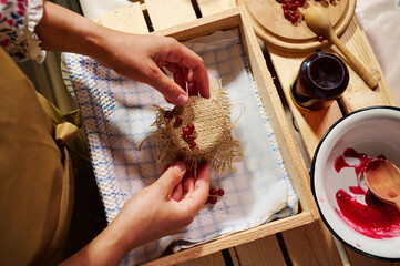 Housewife tying bow on burlap, decorating the cover of a jar with homemade jam