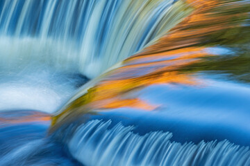 Landscape of a cascade at Bond Falls captured with motion blur and illuminated by reflected color from sunlit autumn maples and blue sky overhead, Michigan's Upper Peninsula, USA