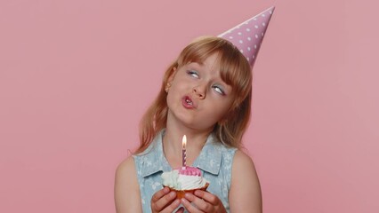 Happy young preteen child girl kid wears festive birthday hat hold cupcake makes wish joyful congratulating blowing burning candle on cake. Little toddler children celebrating anniversary party alone