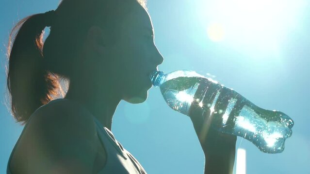 Sporty woman drinking water outdoor on sunny day