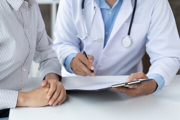 Doctor and patient sitting and talking at medical examination at hospital office, close-up. Therapist filling up medication history records. Medicine and healthcare concept.