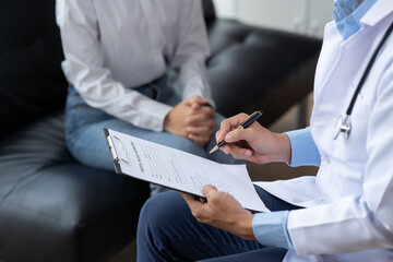 Doctor and patient sitting and talking at medical examination at hospital office, close-up. Therapist filling up medication history records. Medicine and healthcare concept.