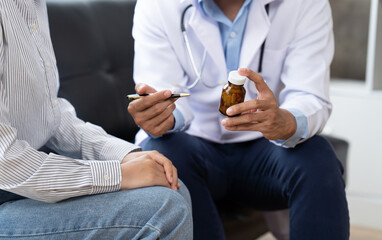 Doctor and patient sitting and talking at medical examination at hospital office, close-up. Therapist filling up medication history records. Medicine and healthcare concept.