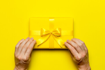 Holiday concept. Male hands holding yellow gift box with bow on yellow background flat lay top...
