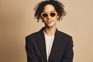 Fototapeta premium Closeup portrait of awesome tanned curly man in classic brown jacket trendy sunglasses posing isolated on beige pastel background. Fashion New Collection offer. Retro style concept. Free place for ad