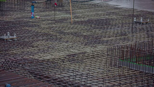 Overview shot of big construction site with workers pouring cement over steel rods in timelapse at daytime.