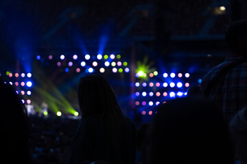 Stage lights against woman enjoying outdoor music festival concert. Silhouette of girl at rock concert crowd in front of bright stage lights.