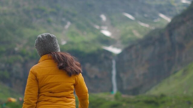 Portrait of Female Indian torist pointing hand towards Sissu Waterfall at Sissu, Lahaul, Himachal Pradesh during monsoon season. Himalayan mountains and waterfall.