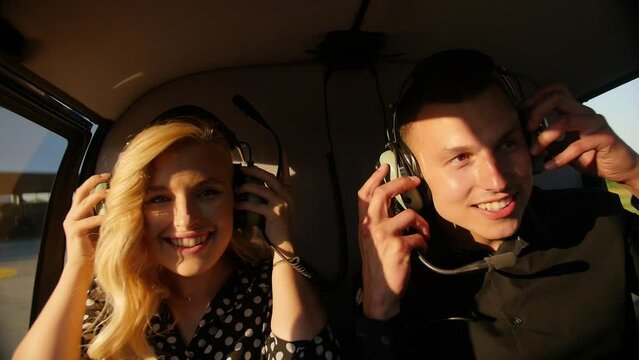 Young couple man and a blonde girl put on headphones to fly in a helicopter.