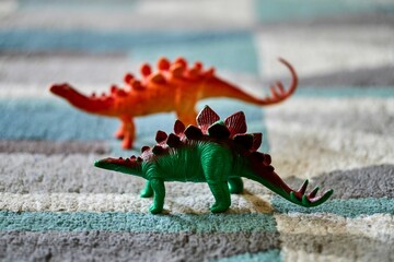 Closeup shot of a green stegosaurus toy on the carpet with a dinosaur toy in the blurred background © Mirco Vacca/Wirestock Creators
