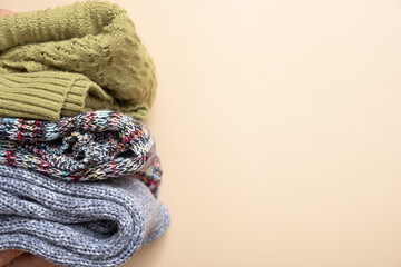 A stack of cozy knitted sweaters on beige background. Warm concept