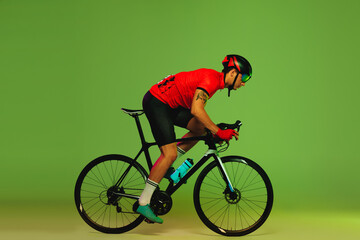 Obraz premium Male cyclist riding bicycle in sports uniform and protective helmet isolated on green studio background. Concept of active life, rest, travel, energy, sport