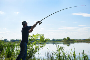 Silhouette of adult fisherman standing by the river and throwing the spinning. Lifestyle. Sport and hobby 