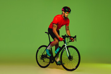 Obraz na płótnie Canvas Young sportsman, cyclist on bicycle in sports uniform and protective helmet training isolated on green background. Concept of active life, rest, travel, energy, sport