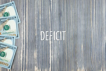 DEFICIT - word (text) on wooden background, money, dollars. Business concept (copy space).