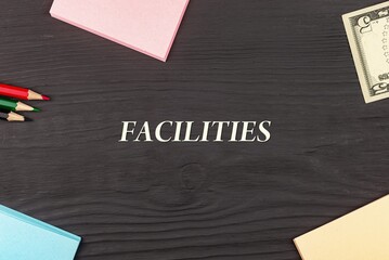 FACILITIES - text, money dollars, stickers and colored pencils on a black wooden table. Business concept: buying, selling, commerce (copy space).