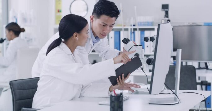 A focused team of researchers working in a laboratory. Young man and woman working at the lab. A guy looking inside a microscope and a girl showing the results or reports.