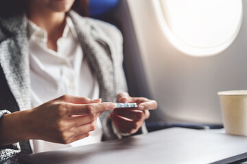 a successful Asian businesswoman or entrepreneur in a formal suit on an airplane in business class taking motion sickness pills during the flight - obrazy, fototapety, plakaty