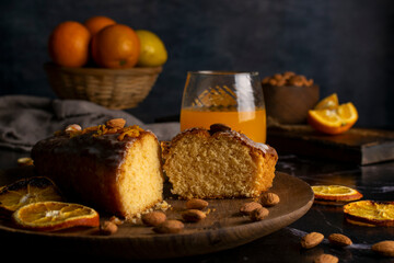 Fototapeta na wymiar orange cake pudding with almonds and whole and sliced natural oranges and orange juice on a dark table