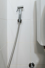 The metal bidet spray is hanging on the white tile wall near the flush toilet.