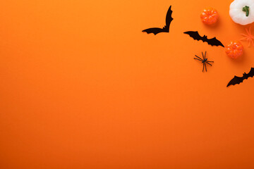 Orange Halloween background. Flock of black bats, spider, pumpkin, skeleton and leaves for Halloween. Black paper bat silhouettes on orange background. Autumn decoration. Halloween concept. Top view.