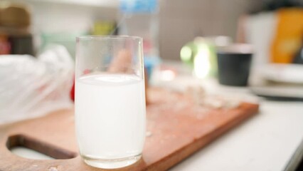 A white cloudy liquid swirls in a clear glass beaker in the foreground in the morning. Yesterday's feast in the background in a blurred background.