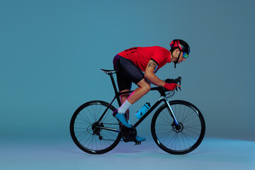 Studio shot of professional cyclist in red sports uniform, goggles and a helmet on a blue background. Concept of active life, rest, travel, energy, sport