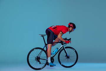 Naklejka premium Studio shot of professional cyclist in red sports uniform, goggles and a helmet on a blue background. Concept of active life, rest, travel, energy, sport