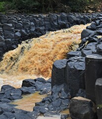 Vertical shot of the muddy water flowing between basalt rock formations.