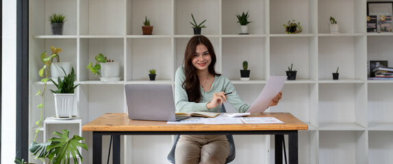 Portrait of businesswoman using laptop computer while working with using a calculator to calculate the numbers, finance accounting concept - banner shot