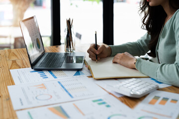 businesswoman or accountant taking note and working on calculator and laptop computer to calculate...