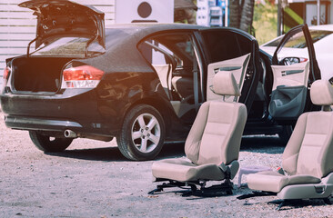 Cream-colored car seats removed from the black car for sun exposure and cleaning in open air.
