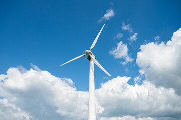 Low angle of wind turbine's giant propellers under the cloudy blue sky