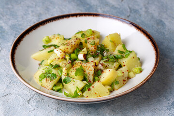 Potato salad with green onion on white plate over wooden background with copy space. Top view.