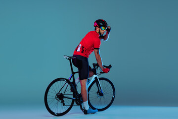 Studio shot of professional cyclist in red sports uniform, goggles and a helmet on a blue background. Concept of active life, rest, travel, energy, sport