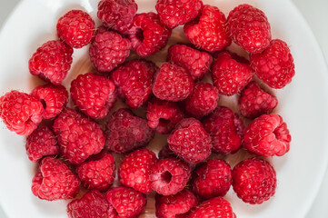Ripe juicy raspberry on a white plate. Raspberry background.
