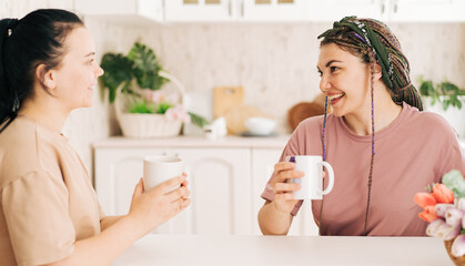 Two girls with mugs of coffee talking at the table.