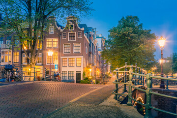 Obraz premium Romantic Amsterdam lit the lights. Evening view of the famous historic center with lantern lights, bridges, canals and cute Dutch houses.