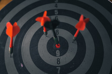 Close up shot of the dart arrow hit on bulleyes of dartboard to represent that the business reached the target of company with dark tone picture style. Target and goal as concept. 