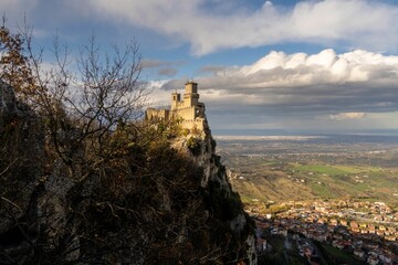 View of the Guaita fortress on the mountain edge against the cloudy blue sky. San Marino, Italy.