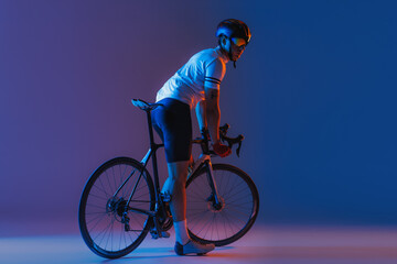 One male cyclist riding bicycle wearing cycling shorts and protective helmet isolated on dark blue...