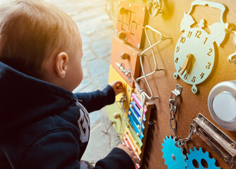 A little boy is playing with a busy board. Developming toy for children from one year old....