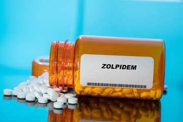 Zolpidem white medical pills and tablets spilling out of a drug bottle. Macro top down view with...