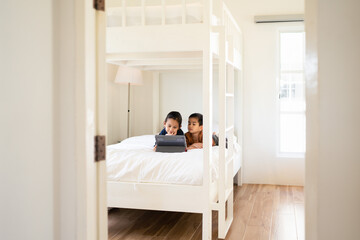 Asian little sibling watching video clip on tablet together in the bedroom with happy moment. Concept of technology, internet, social media, conncection, learning, education and homeschool for kid.