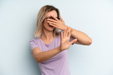 young adult pretty woman covering face with hand and putting other hand up front to stop camera,...
