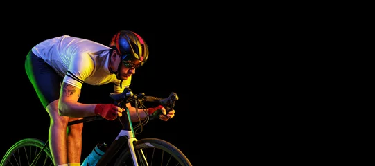 Plexiglas foto achterwand Flyer with male cyclist riding bicycle wearing cycling shorts and protective helmet isolated on dark background in neon. Concept of sport, speed, energy © master1305