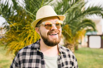 Laughing attractive man wearing hat over palm tree background - emotion and vacation travel holidays concept