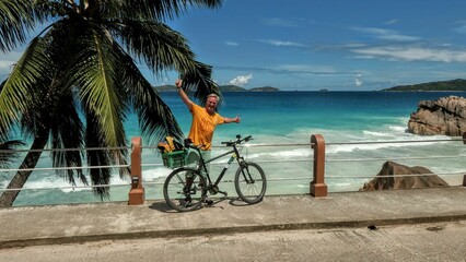 Closeup of a male Caucasian leaning on the coastal barrier with his bicycle in La Digue, Seychelles