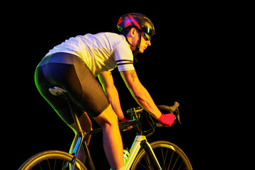 Portrait of young male cyclist on bicycle in cycling shorts and protective helmet isolated on dark...